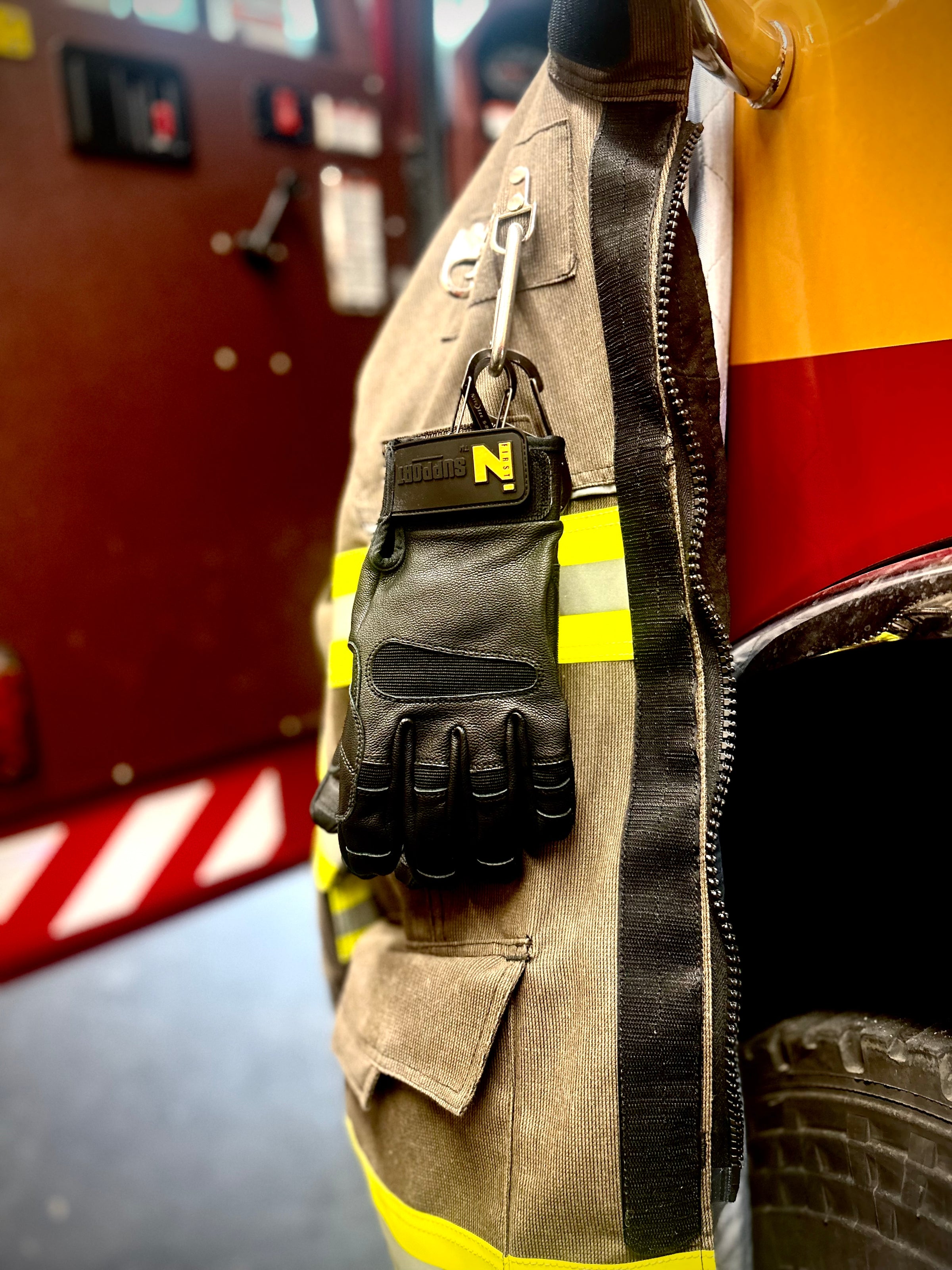 FIRST IN - SUPPORT gloves hanging from a carabiner attached to the firefighters jacket.