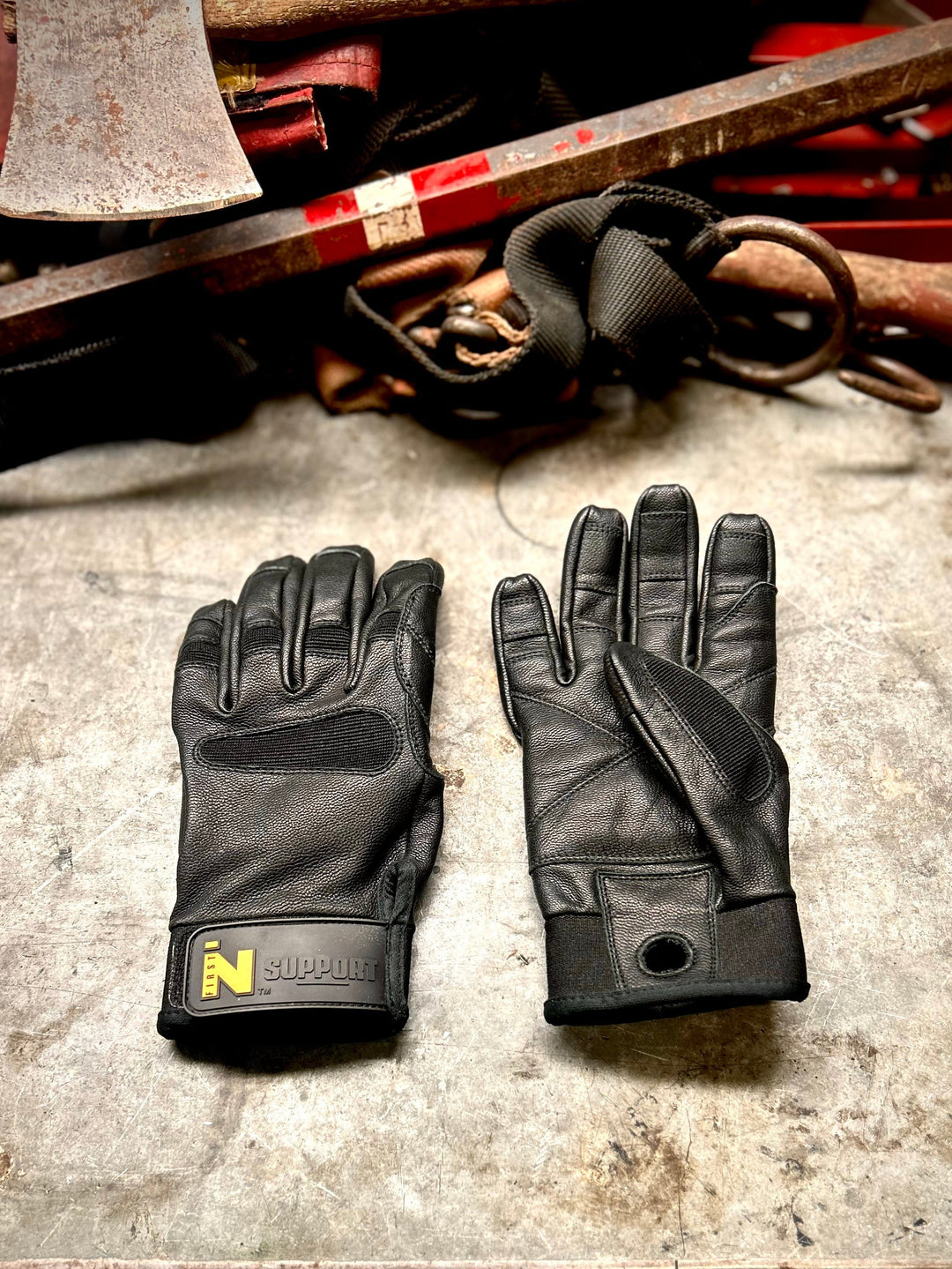 FIRST IN - SUPPORT gloves on a workbench. One lays face up, the other lays face down next to it.