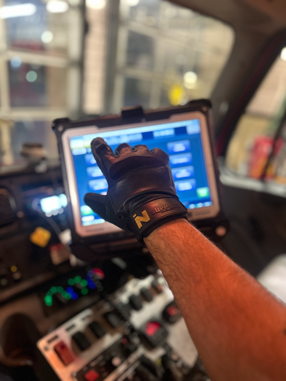 A firefighter wearing a FIRST IN - SUPPORT glove interacting with a touch screen inside a fire truck.